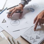 Finger pointing to a note book with right and on a drawing of logos to prepare brand guidelines to instruct on trademark use